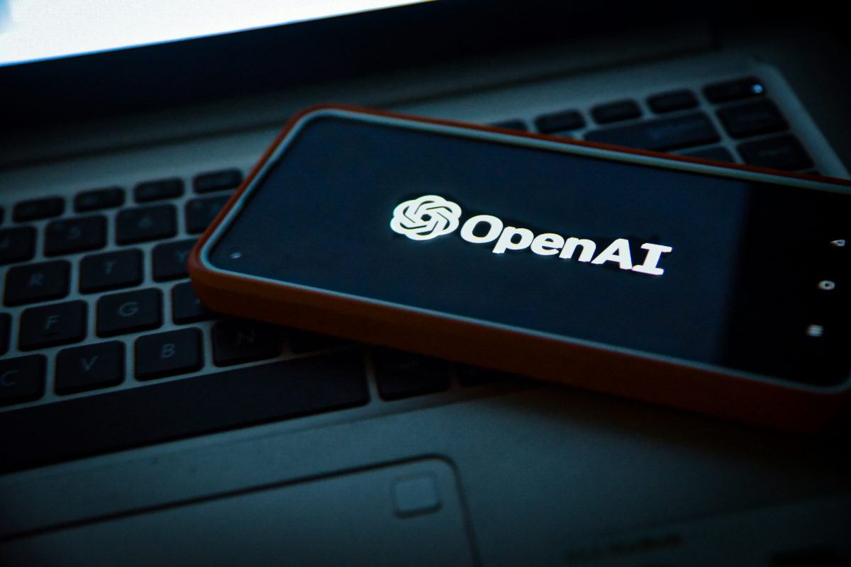 Логотип OpenAI на экране смартфона на фоне ноутбука
