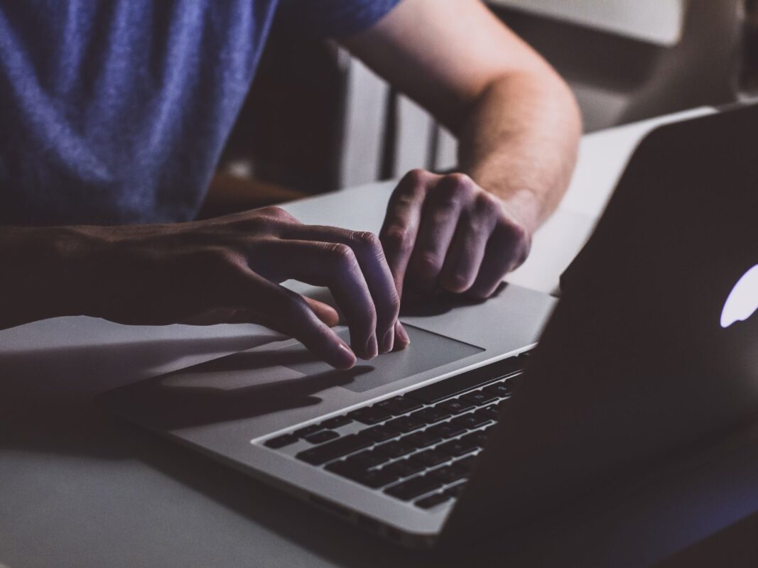 Руки за клавиатурой MacBook в темноте, светящийся логотип Apple