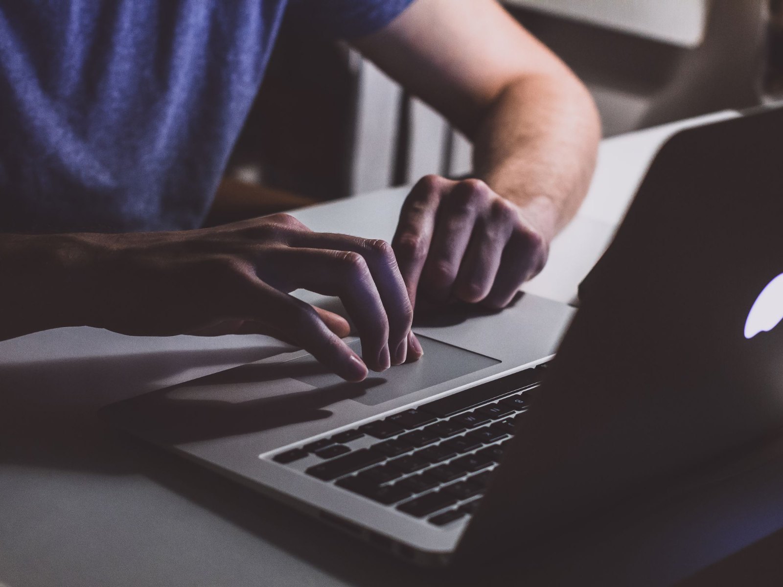Руки за клавиатурой MacBook в темноте, светящийся логотип Apple