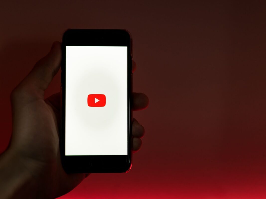 Смартфон с логотипом YouTube на красном фоне в руке