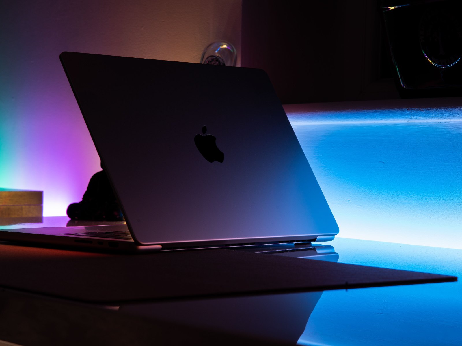 Полуоткрытый MacBook в тёмной комнате, свет из щели падает на стол