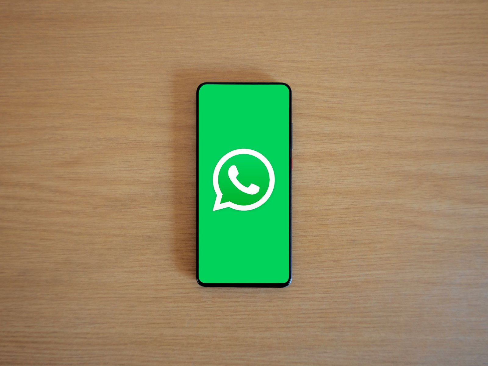 Смартфон на деревянном столе с экраном запуска WhatsApp и логотипом